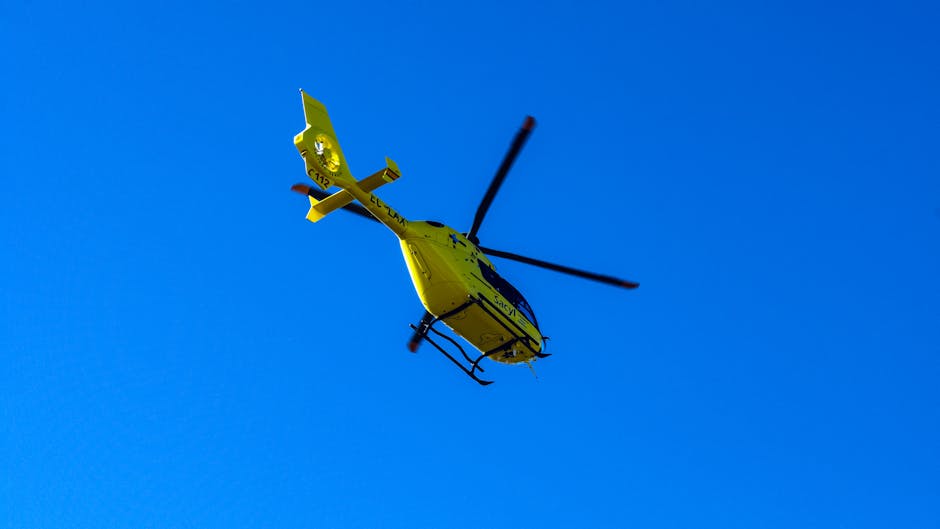 A medium-sized rescue helicopter with a predominantly white fuselage featuring green and yellow accents, flying against a clear blue sky. The helicopter's tail and vertical stabilizer display a checke