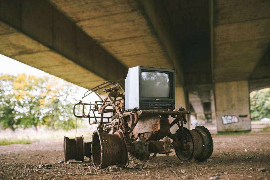 In a dimly lit industrial or storage area with concrete walls and flooring, three washing machines are stacked against the wall, with one positioned directly on the floor and the other two placed on t